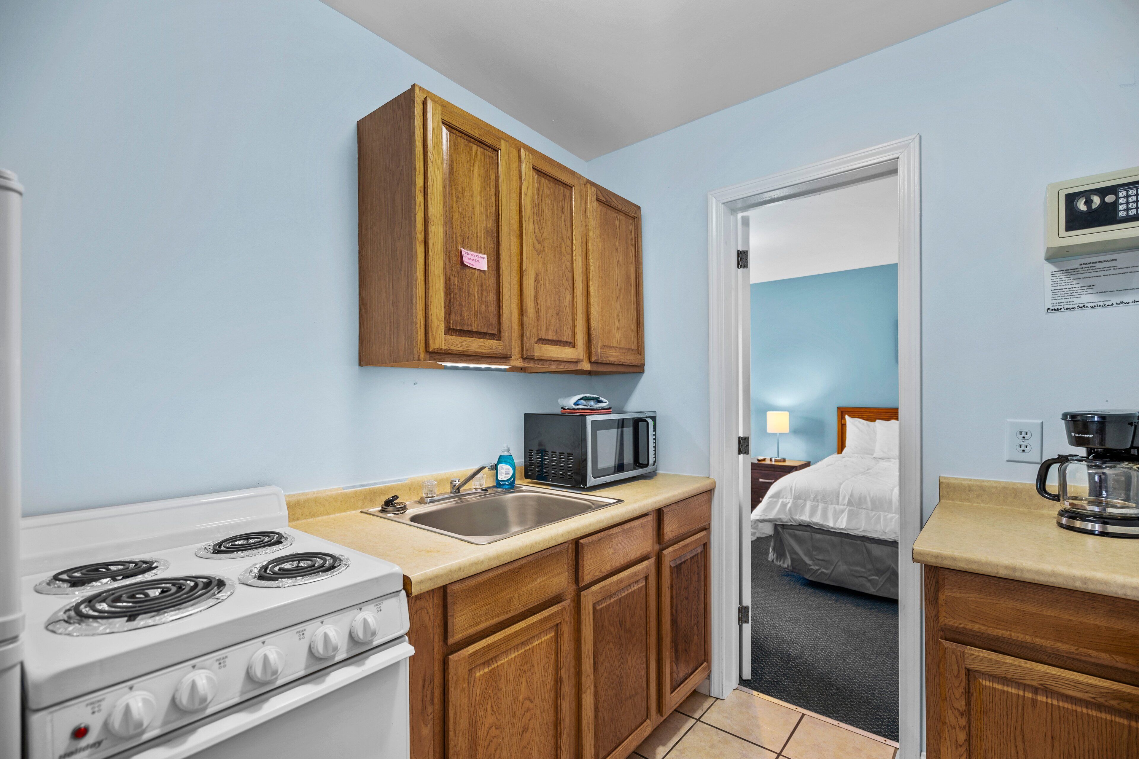 A compact kitchen with wooden cabinets, a microwave, a stove, and a coffee maker.