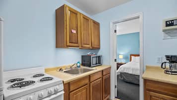 A compact kitchen with wooden cabinets, a microwave, a stove, and a coffee maker.