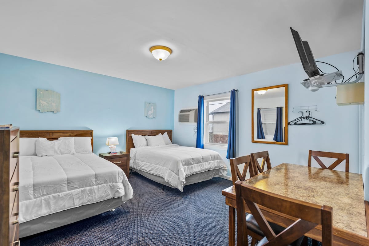 Quarto de hotel com duas camas, uma mesa de jantar e uma televisão fixada na parede.