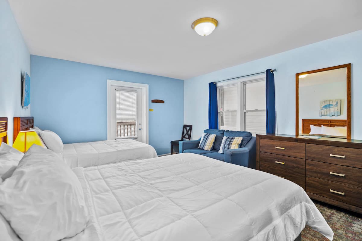 Quarto com duas camas, cômoda, mesa de cabeceira e janela com cortinas.