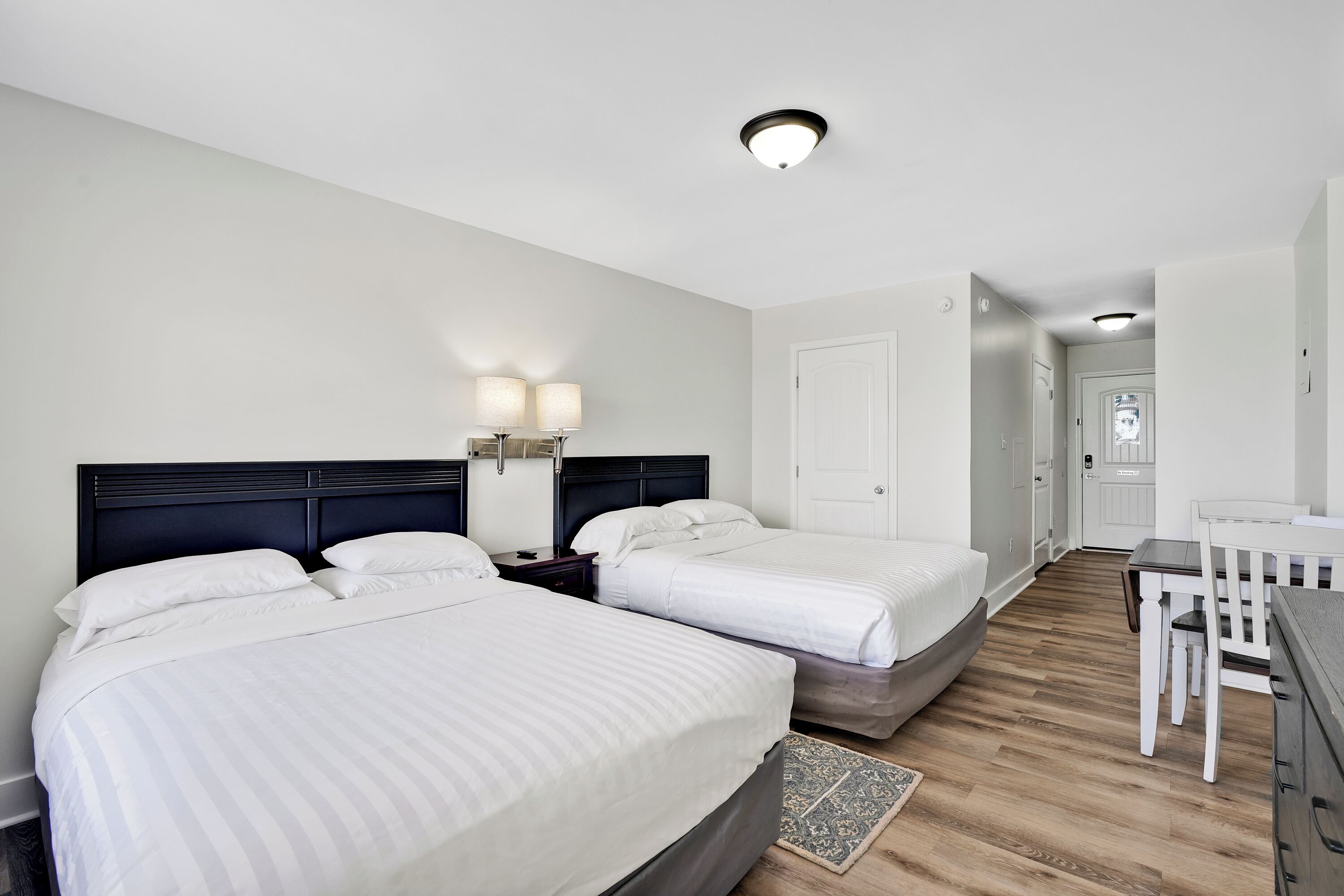 A hotel room with two beds, a desk, a chair, and a small rug.