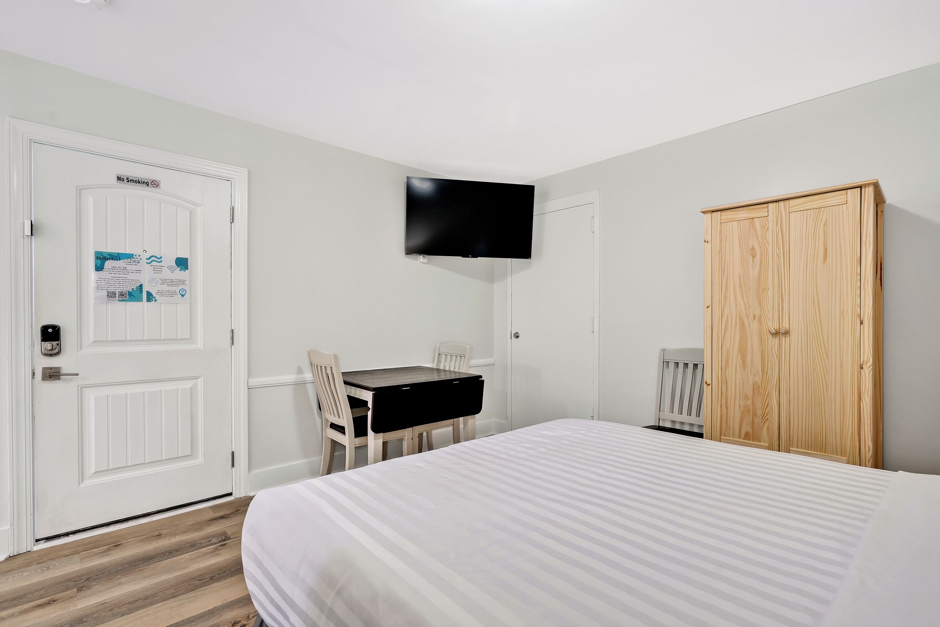 A hotel room with a bed, a desk with chairs, a television mounted on the wall, and a wardrobe.