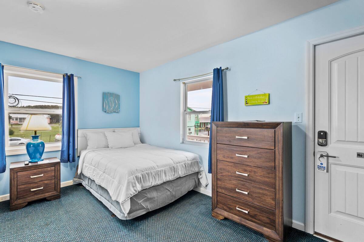 Quarto com cama, penteadeira, mesa de cabeceira e janela com cortinas.