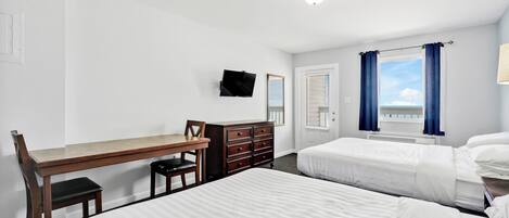 A hotel room with two beds, a desk, a dresser, a TV, and a window with curtains.