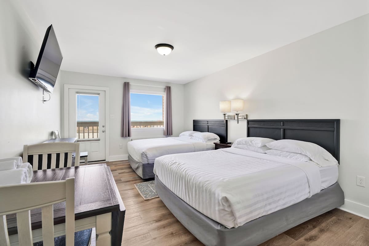 Quarto de hotel com duas camas, uma escrivaninha, televisão na parede e uma janela com cortinas.