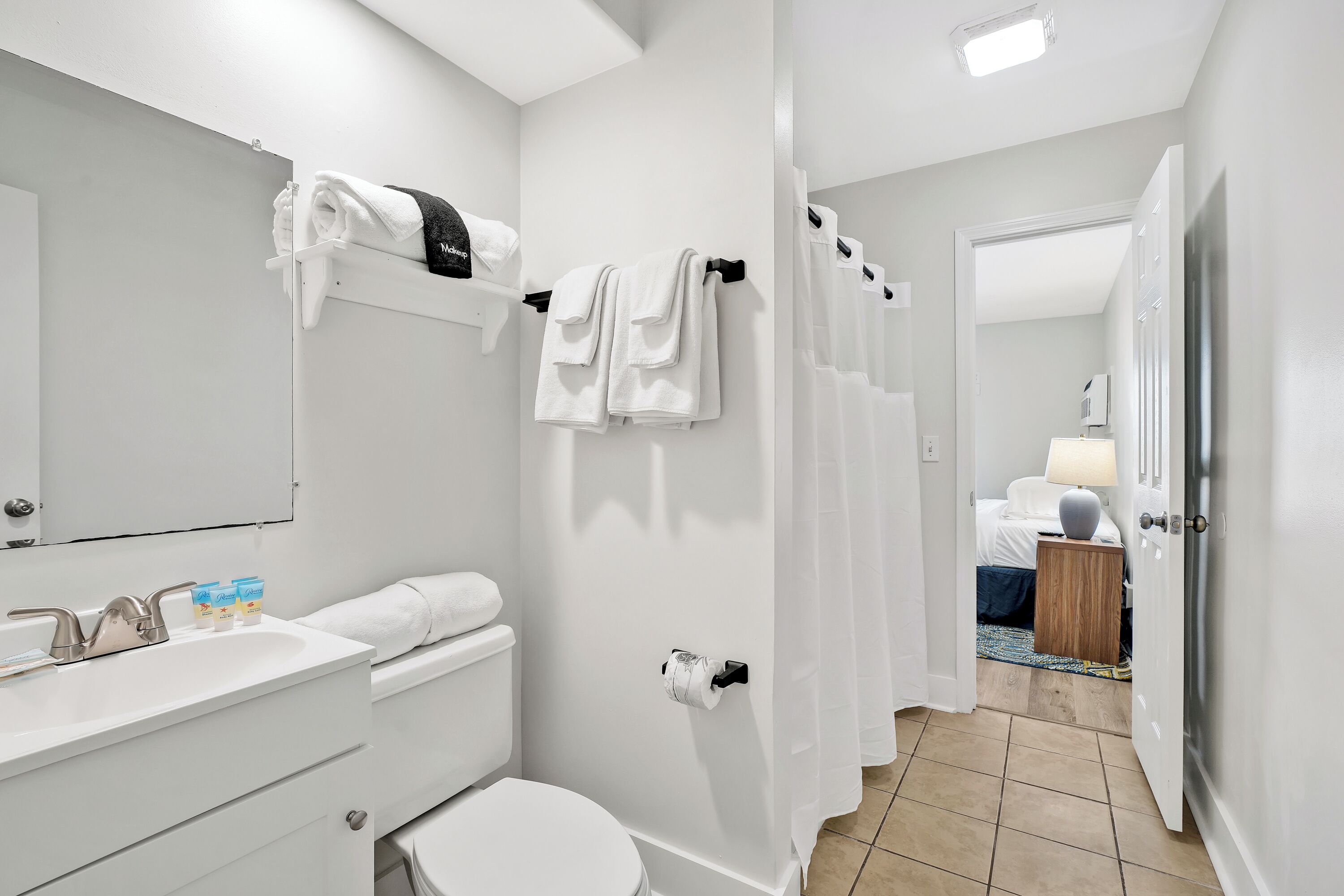 Ein modernes Badezimmer mit Waschbecken, Toilette und Duschvorhang. Auf der Ablage liegen Handtücher und Pflegeprodukte.