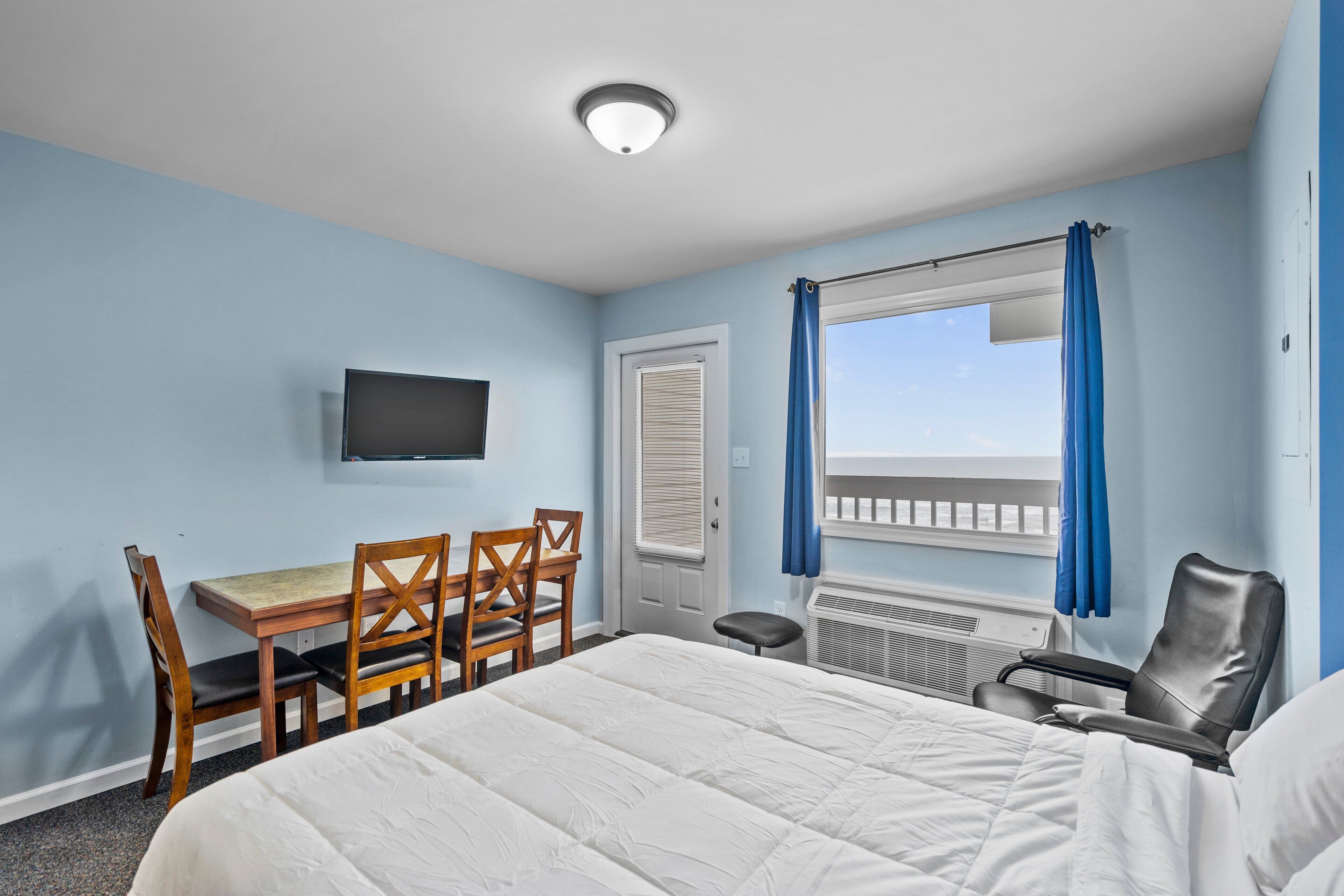A hotel room with a bed, a desk with chairs, a television, and a window with curtains.