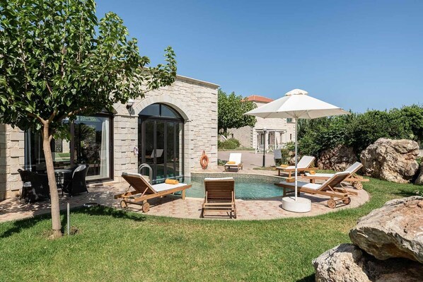 Un espace piscine avec des chaises longues et un bâtiment en pierre doté d’une porte en verre.