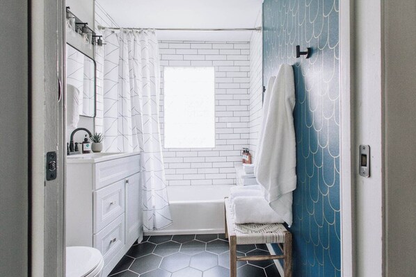 A bathroom with a white toilet, a sink with a mirror, a shower with a white curtain, a bathtub, and a towel rack.