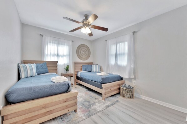 Un dormitorio con dos camas de madera, un ventilador de techo y un adorno en la pared.
