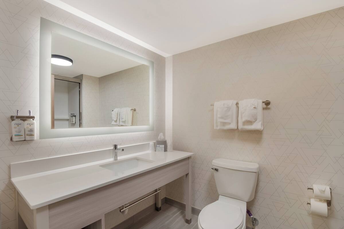 A modern bathroom with a white sink, mirror, and toilet. There are two towels hanging on the wall.