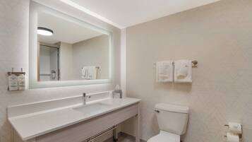 Une salle de bain moderne avec un lavabo blanc, un miroir et des toilettes. Deux serviettes sont accrochées au mur.