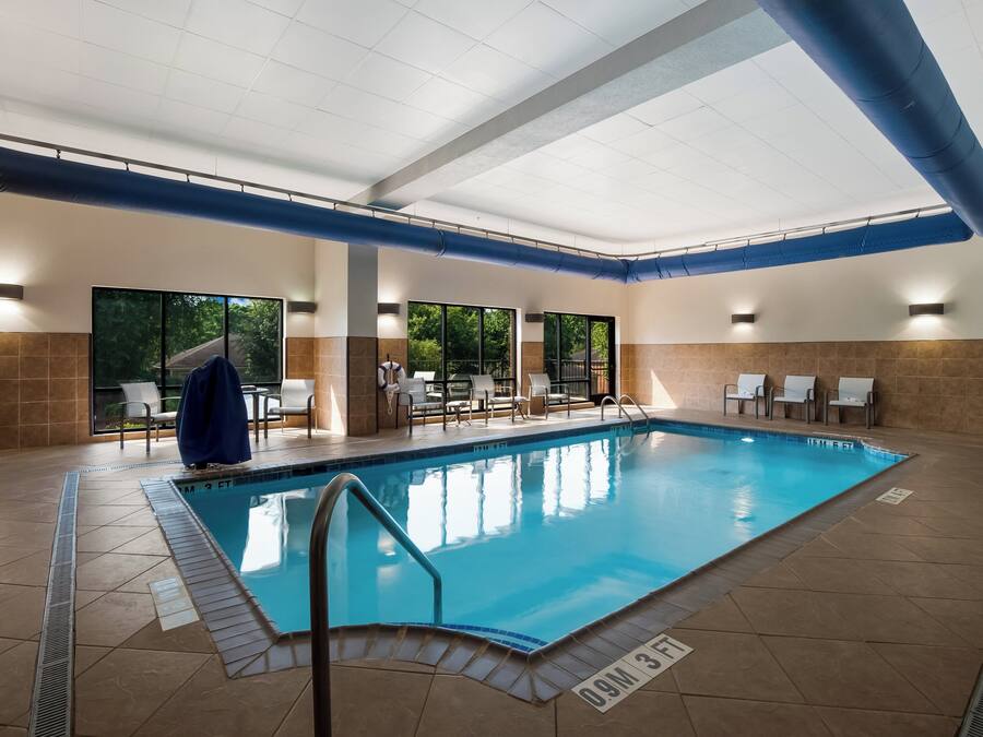 Piscina interior com água cristalina, rodeada por paredes azulejadas e teto com canos azuis.