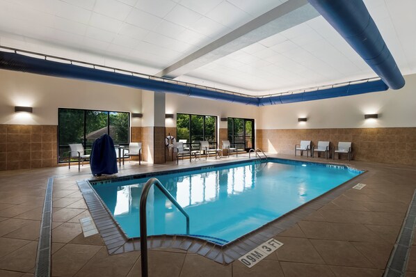 An indoor swimming pool with clear water, surrounded by tiled walls and a ceiling with blue pipes.