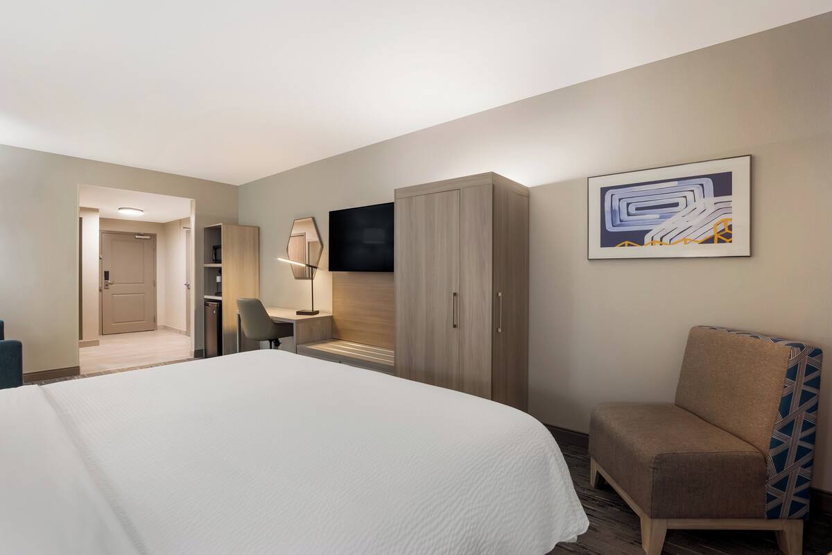 A hotel room with a large bed, a desk with a chair, a wardrobe, and a TV on the wall.