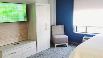 A hotel room with a bed, a TV on the wall, a wardrobe, a chair, and a window.