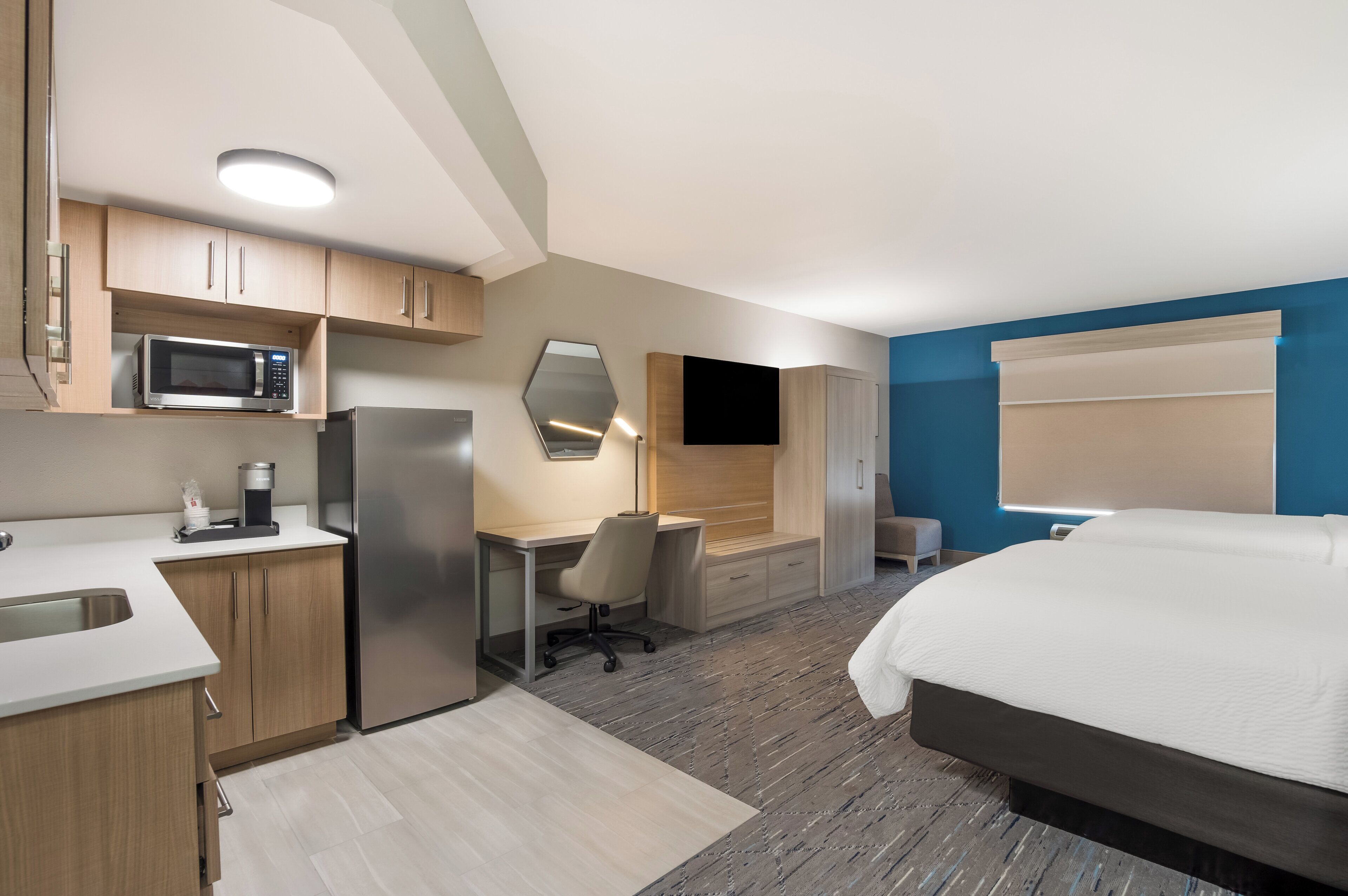Une chambre d’hôtel moderne équipée d’une kitchenette, d’un lit, d’un bureau et d’une télévision.