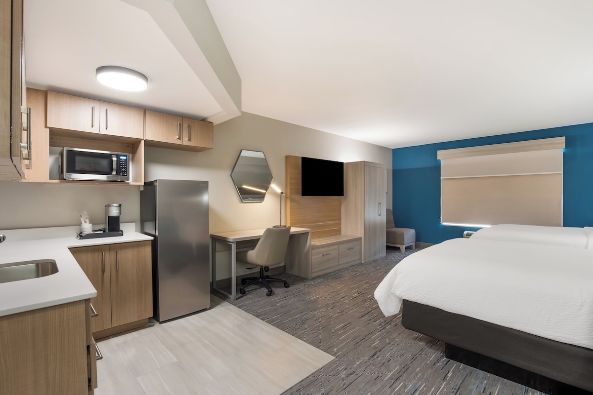 A modern hotel room with a kitchenette, a bed, a desk, and a TV.