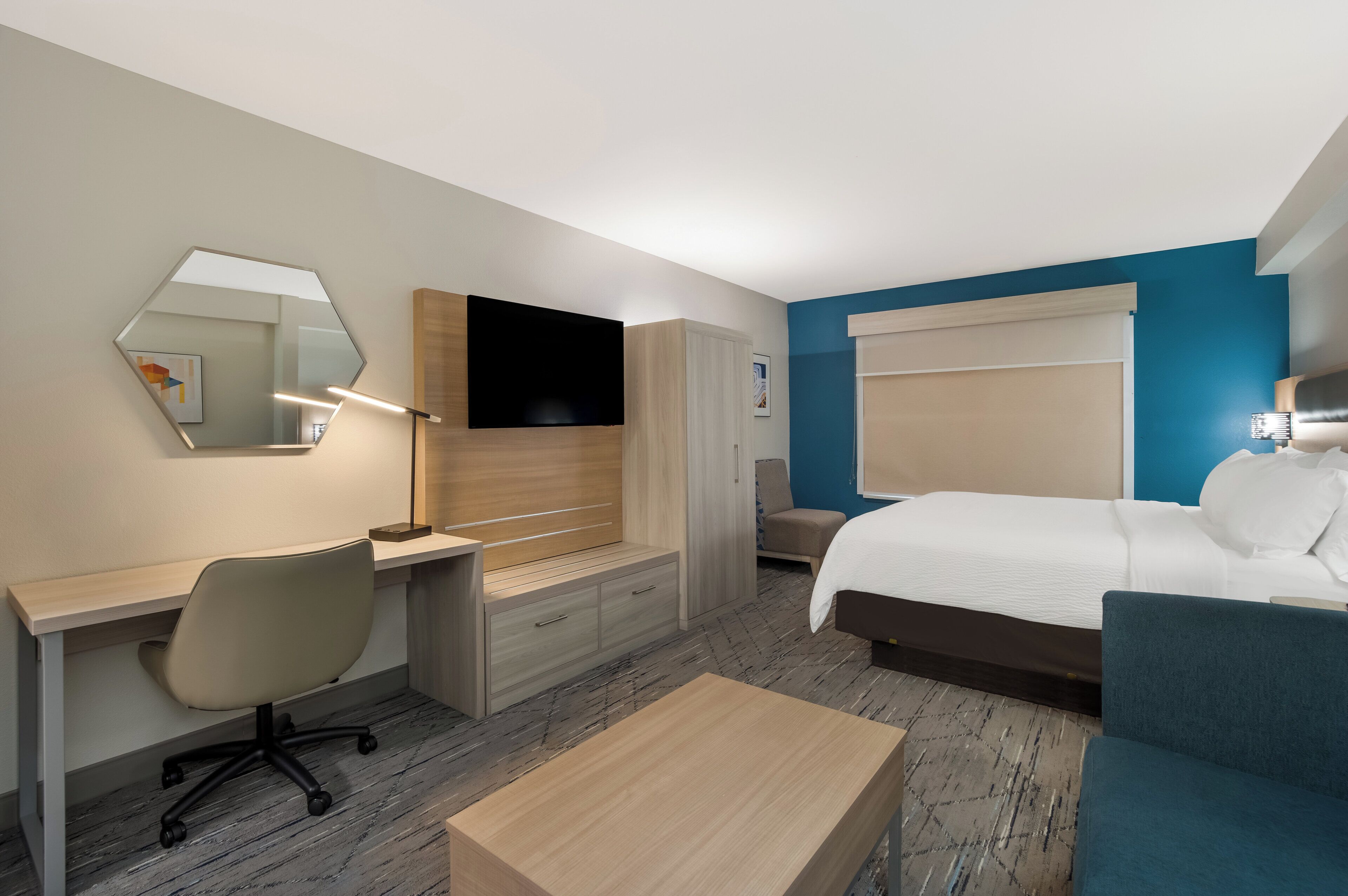 A hotel room with a bed, a desk with a chair, a TV, and a mirror.