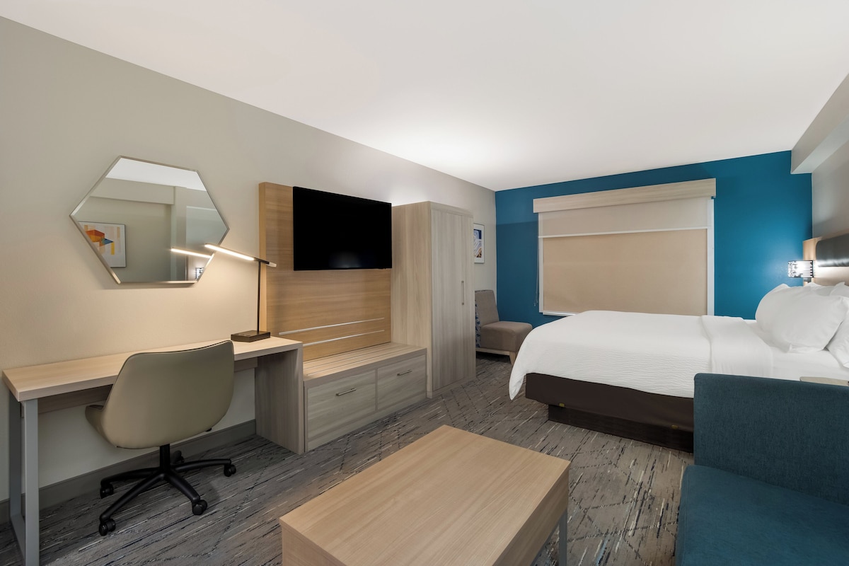 A hotel room with a bed, a desk with a chair, a TV, and a mirror.
