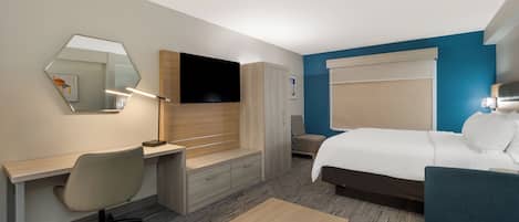 A hotel room with a bed, a desk with a chair, a TV, and a mirror.