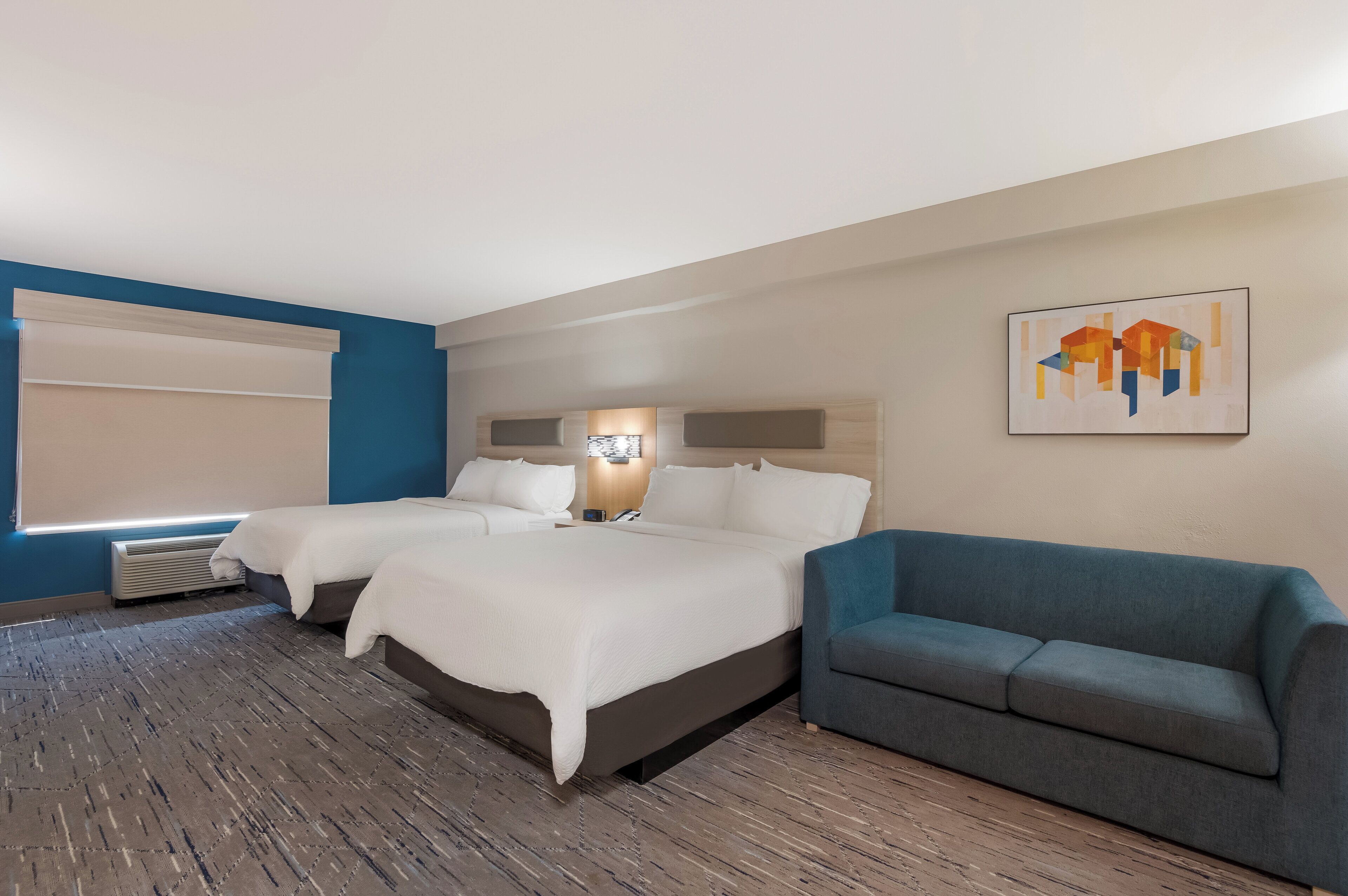 Een hotelkamer met een groot bed, twee nachtkastjes, een blauwe fauteuil en een schilderij aan de muur.