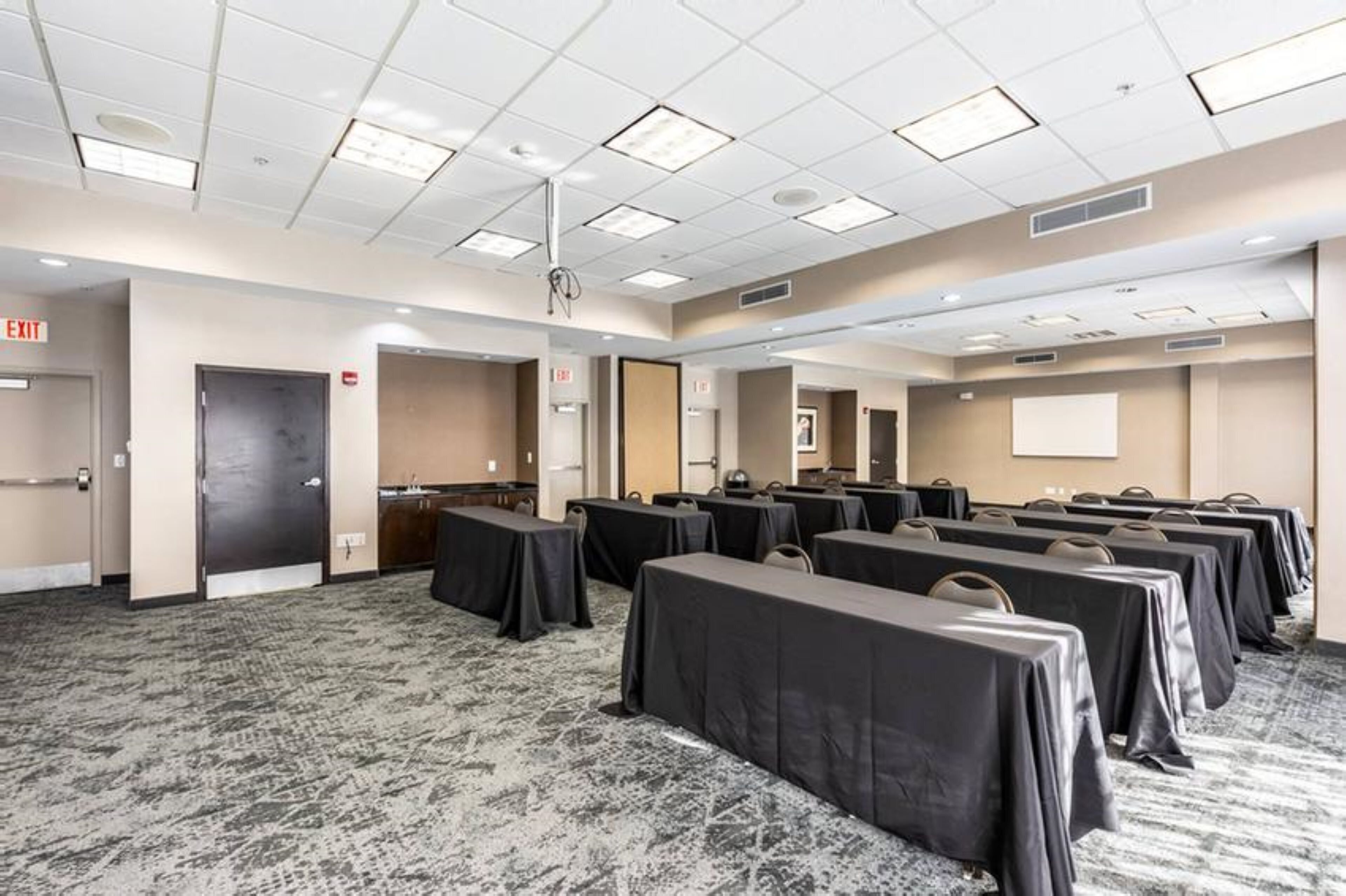 A conference room with multiple tables, carpeted flooring, and ceiling lights.