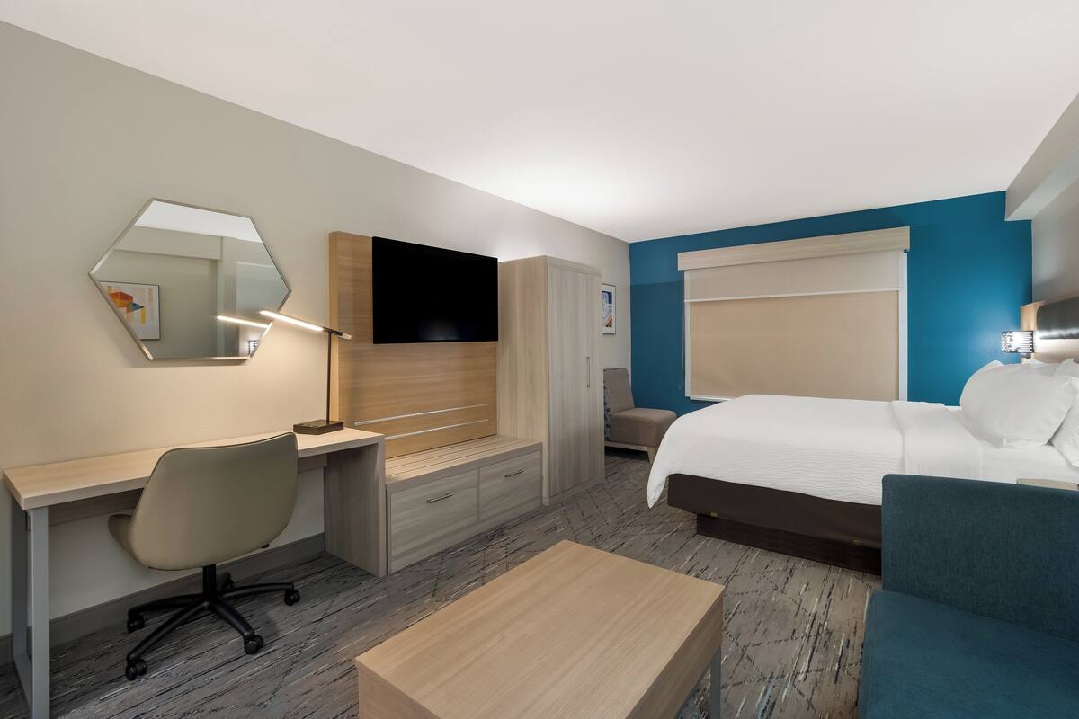 A hotel room with a bed, a desk with a chair, a TV, and a mirror.