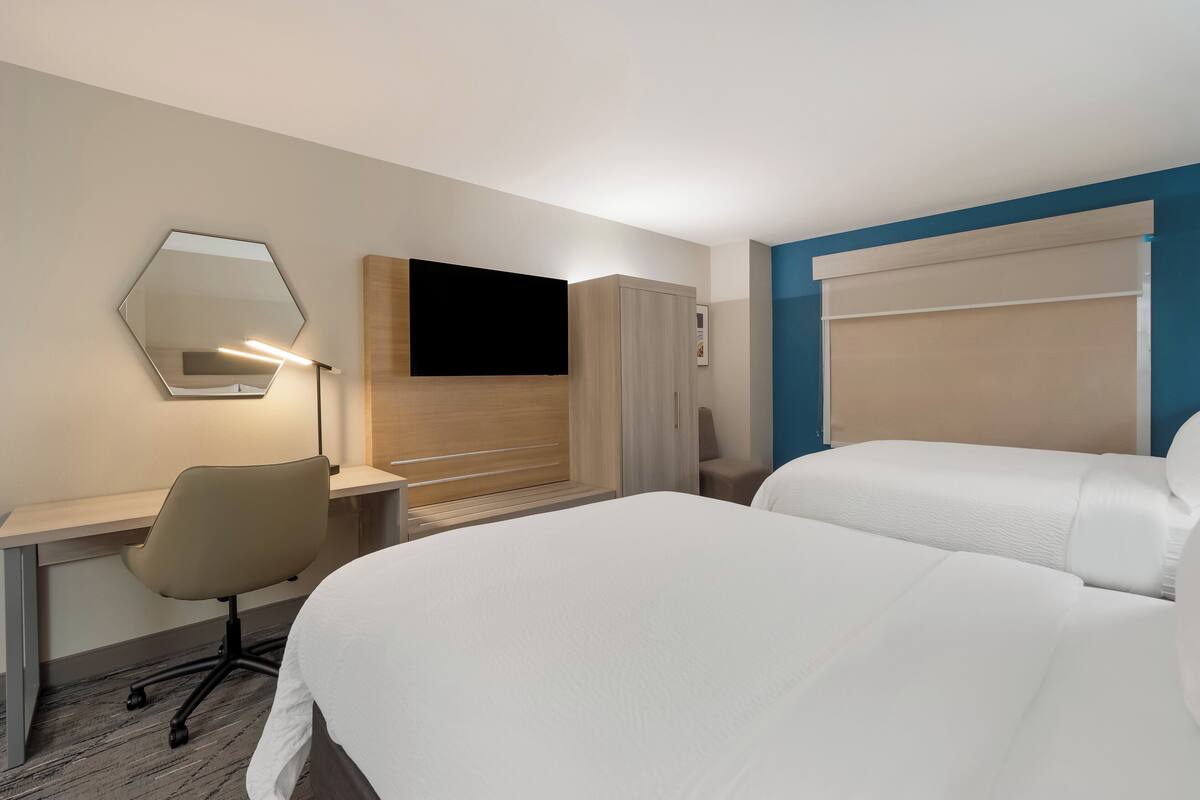 A hotel room with a bed, a desk with a chair, a TV, and a wardrobe.