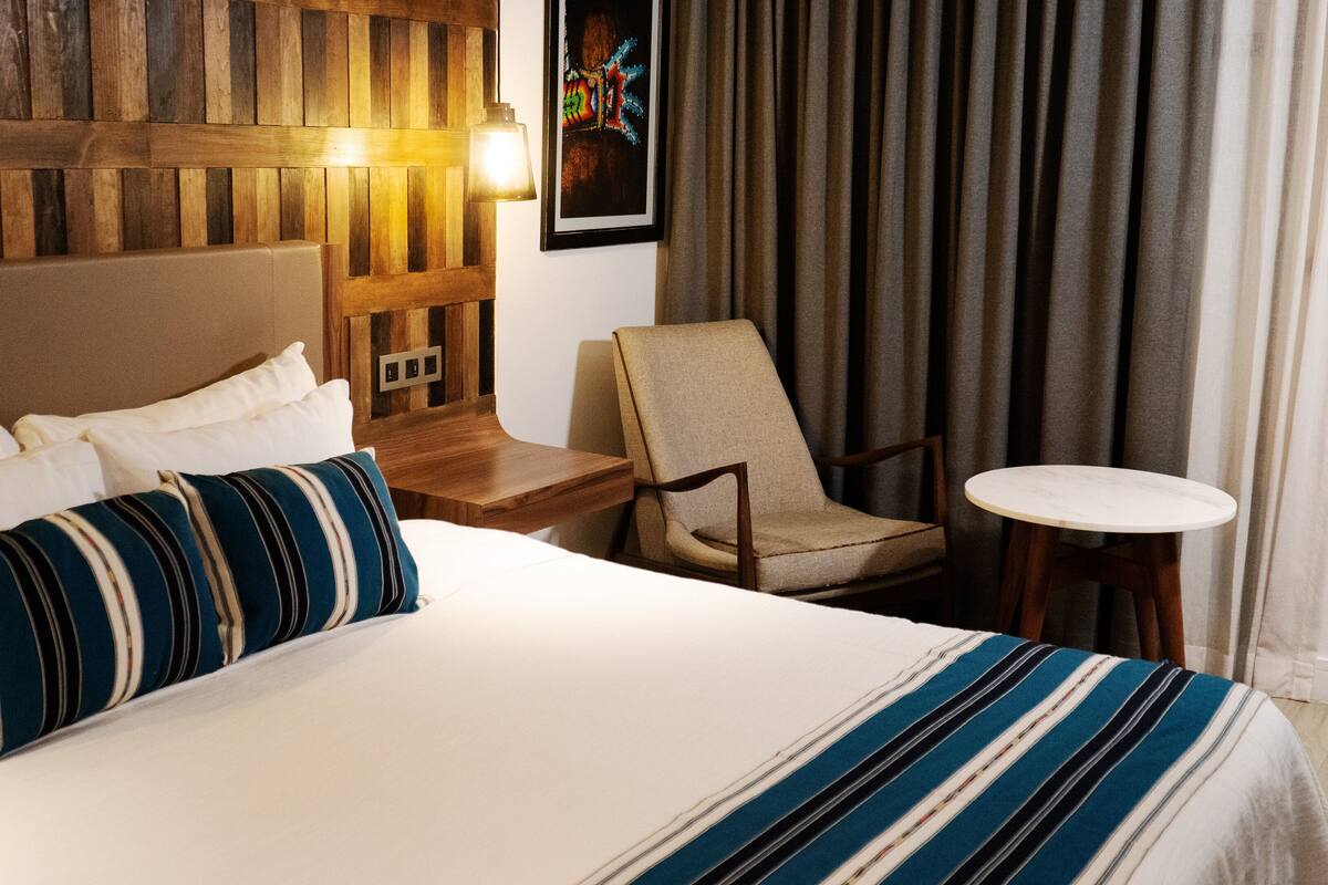 Een hotelkamer met een groot bed, een stoel, een tafeltje en een wandlamp.