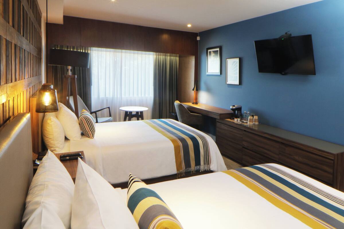Een hotelkamer met twee bedden, een bureau, een televisie en een raam met gordijnen.