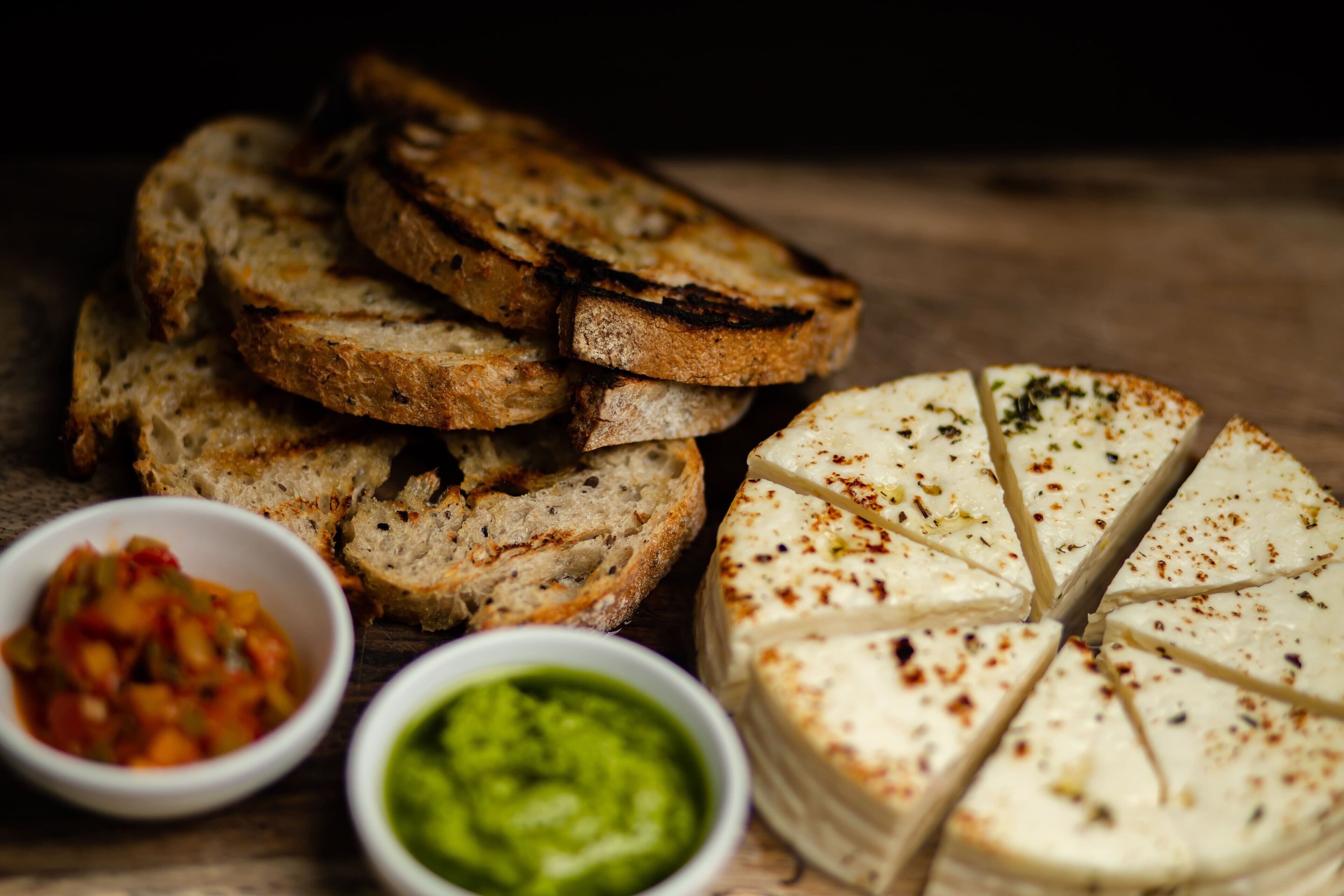 Una rueda de queso y rebanadas de pan con dos recipientes pequeños de salsas.