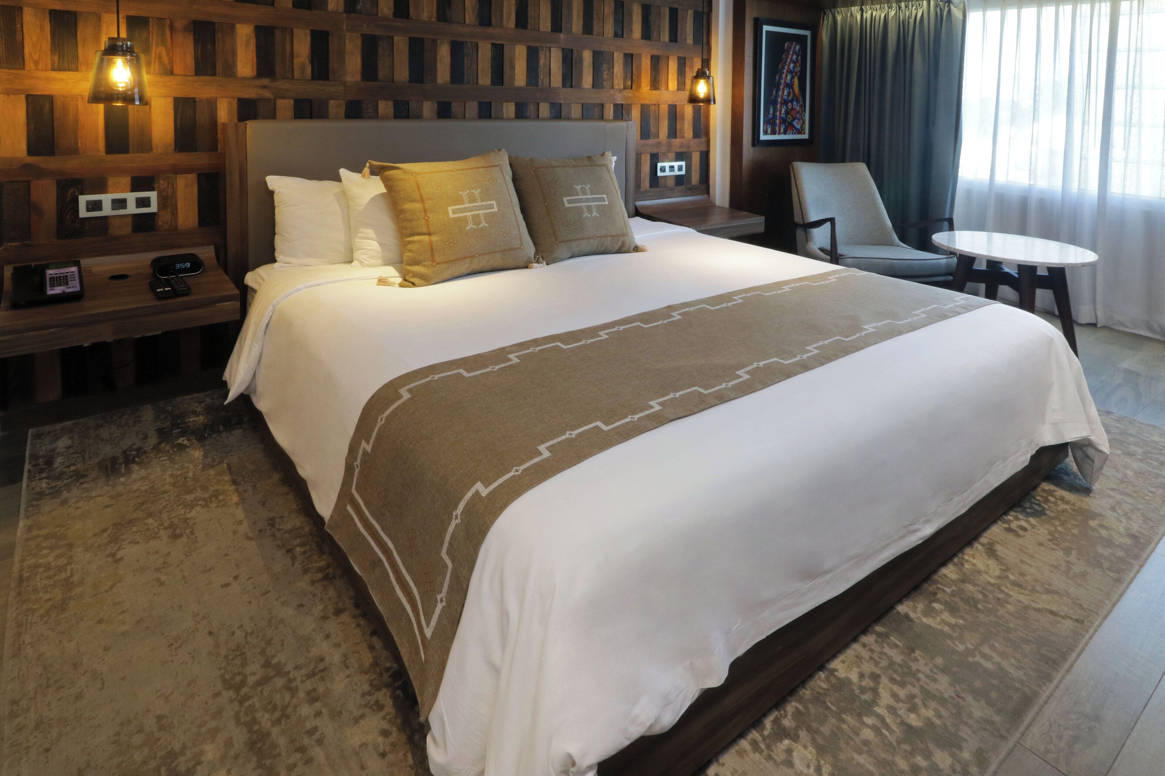Ein Hotelzimmer mit einem großen Bett, einem Nachttisch mit Lampe, einem Sessel und einem kleinen Tisch.