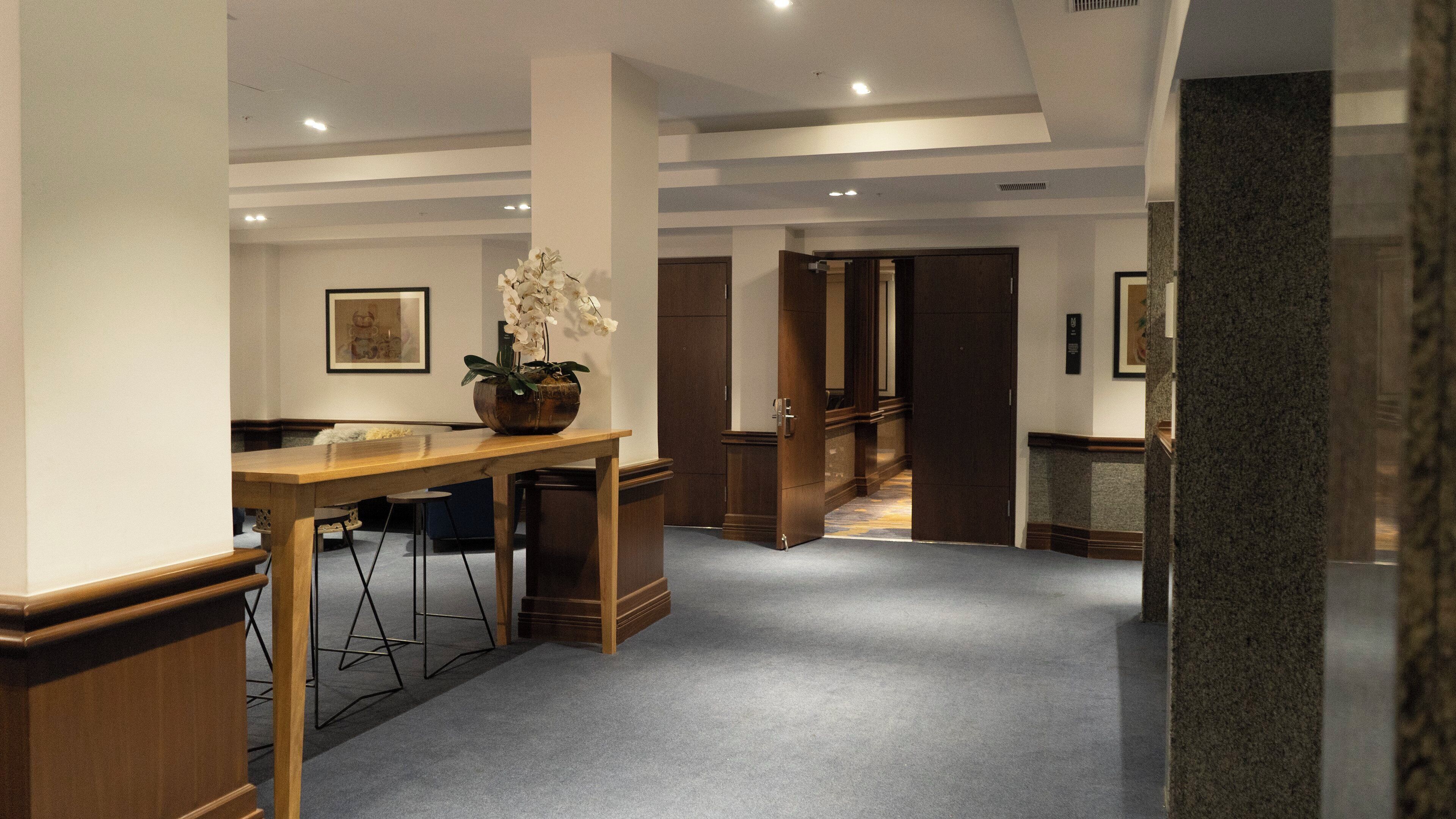 A hotel lobby with a wooden reception desk, a vase of white flowers, and a framed picture on the wall.