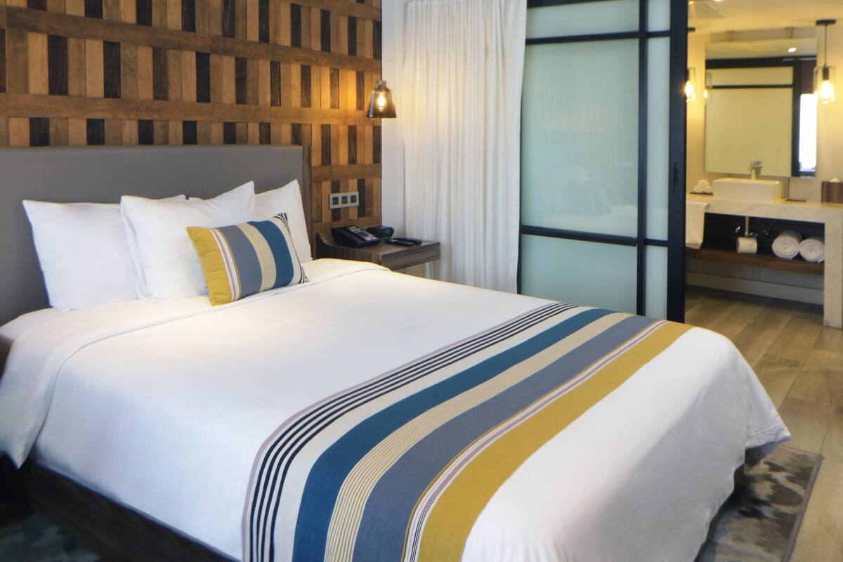 Hotelkamer met een groot bed, een houten hoofdbord, een nachtkastje met telefoon en een badkamer met wastafel en spiegel.