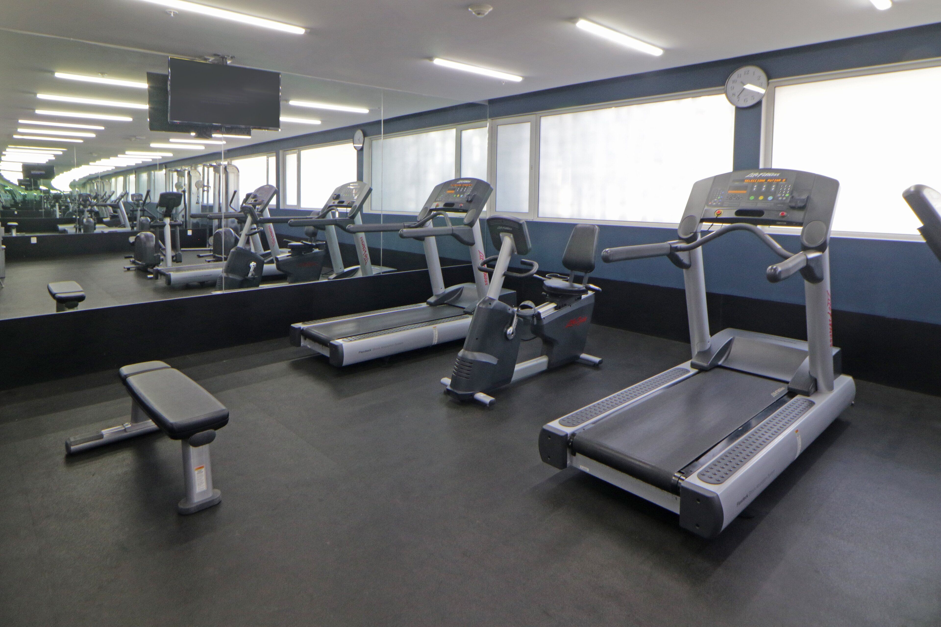 A gym with treadmills, a bench, and a large mirror.