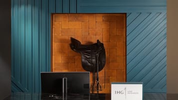 A reception desk with a laptop, a sign reading "IHG ONE REWARDS", and a wooden door with a brick wall behind it.