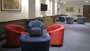 Um saguão de hotel com balcão de recepção, uma televisão de tela plana e várias poltronas.