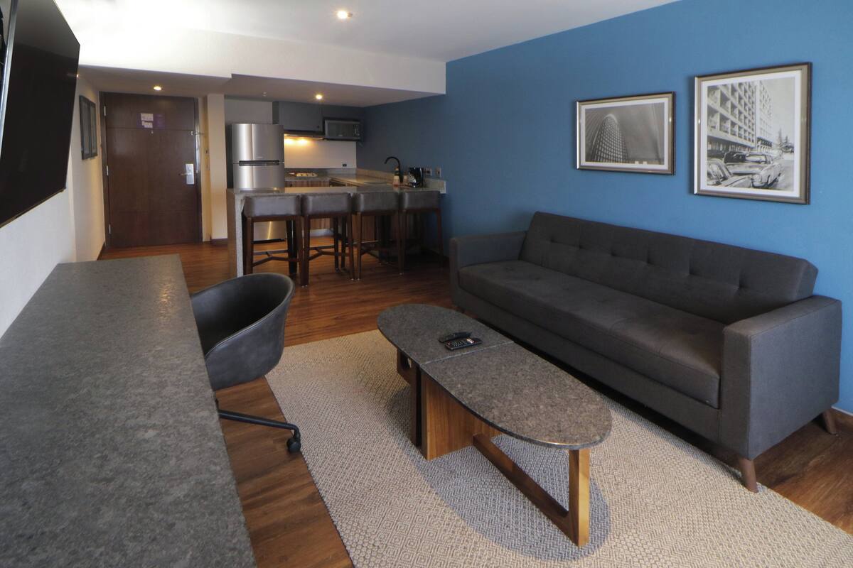 Een moderne woonkamer met een grijze bank, een salontafel en een keuken op de achtergrond.