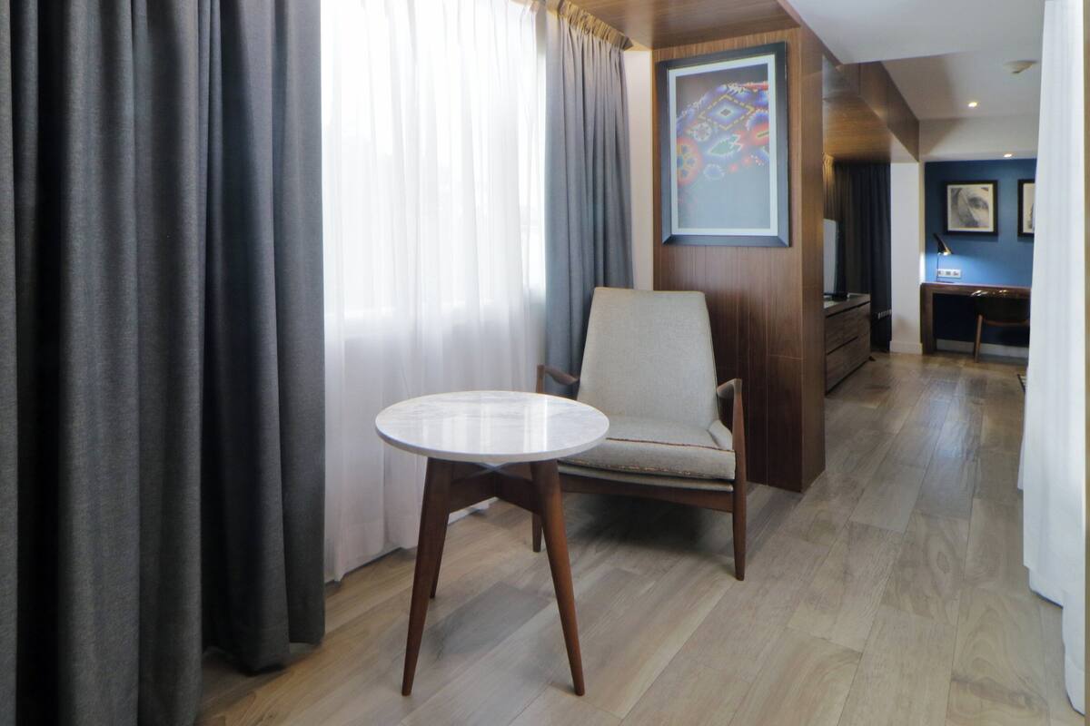 Een moderne hotelkamer met een ronde tafel, een comfortabele fauteuil en een houten bureau.