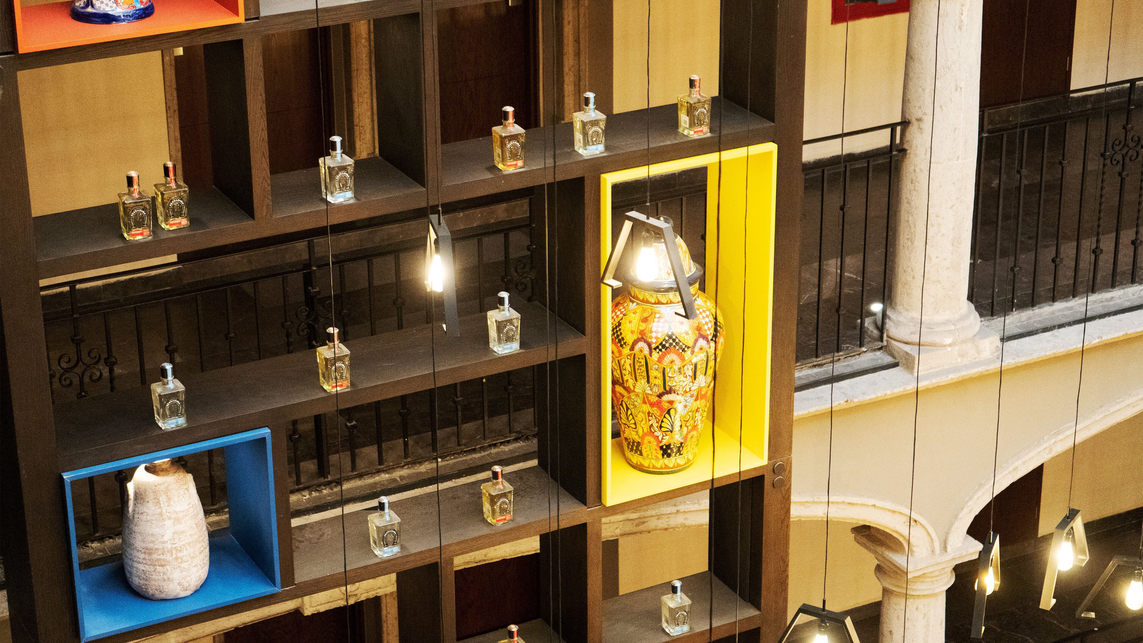 Exposição de diversos frascos de perfume em prateleiras, um vaso decorativo e luminárias pendentes.