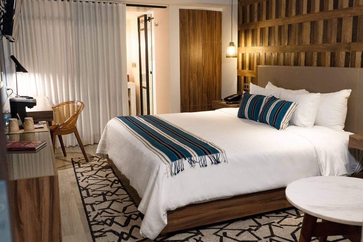 Een hotelkamer met een groot bed, een nachtkastje, een stoel, een bureau met lamp en een kamerkleed met patroon.