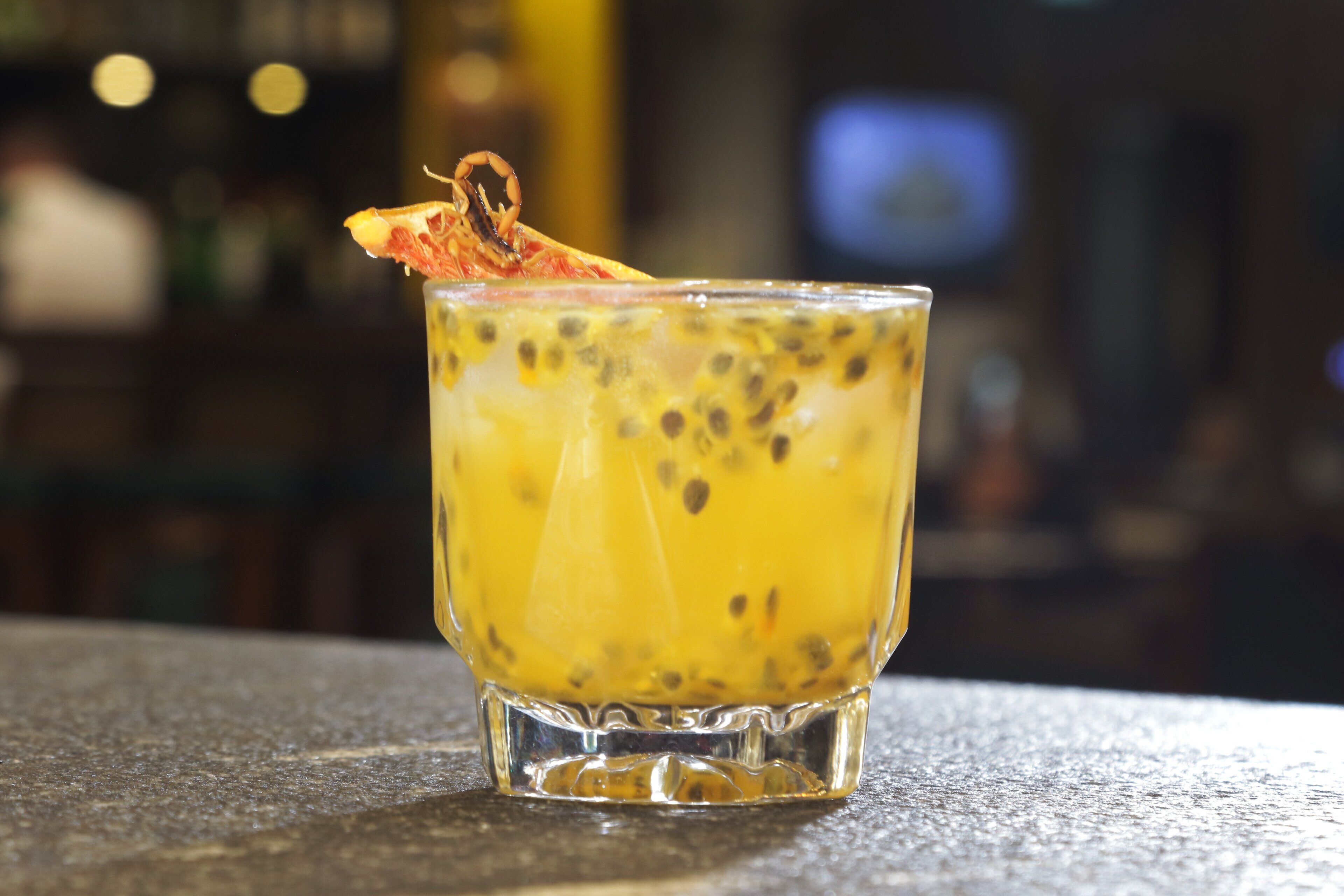 A glass of yellow drink with a garnish on a bar counter.