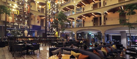 A spacious hotel lobby with multiple seating areas, a bar, and a large collection of decorative items on the walls.
