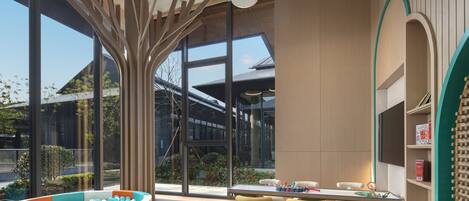 A modern indoor space with a pool table, seating area, and large windows offering views of the outside.