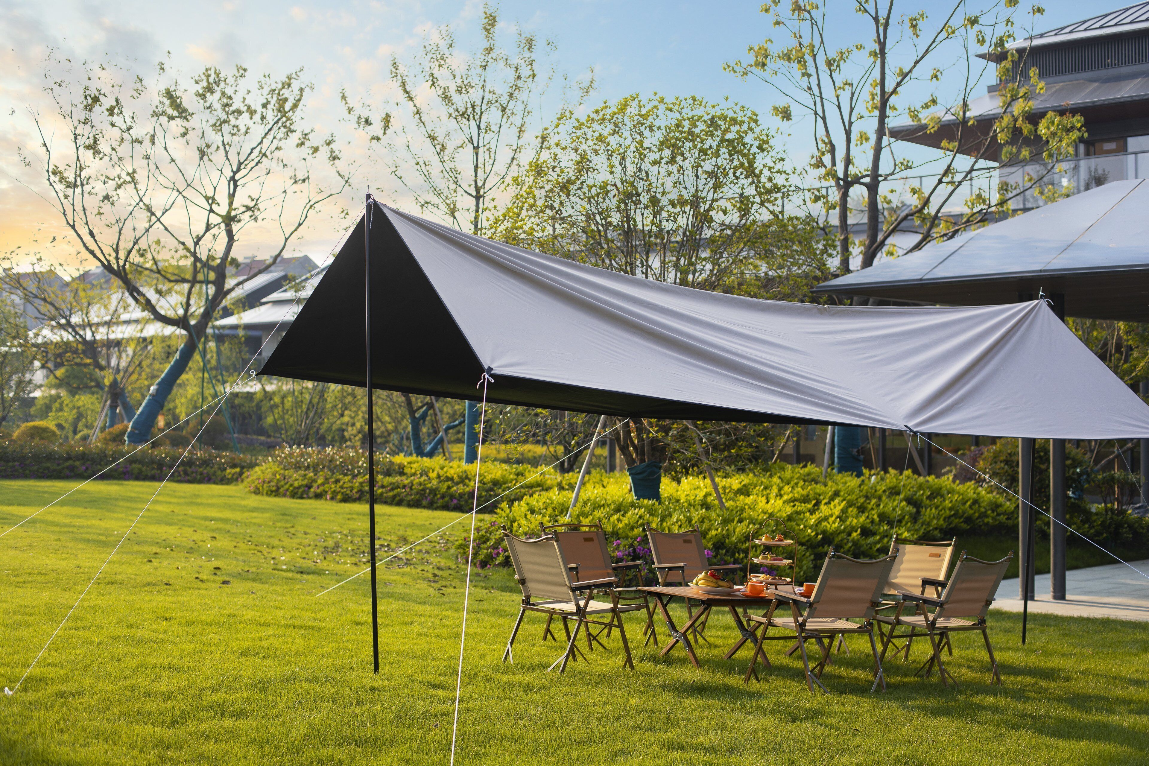 A tented outdoor dining area with a table and chairs, surrounded by a grassy lawn and trees.