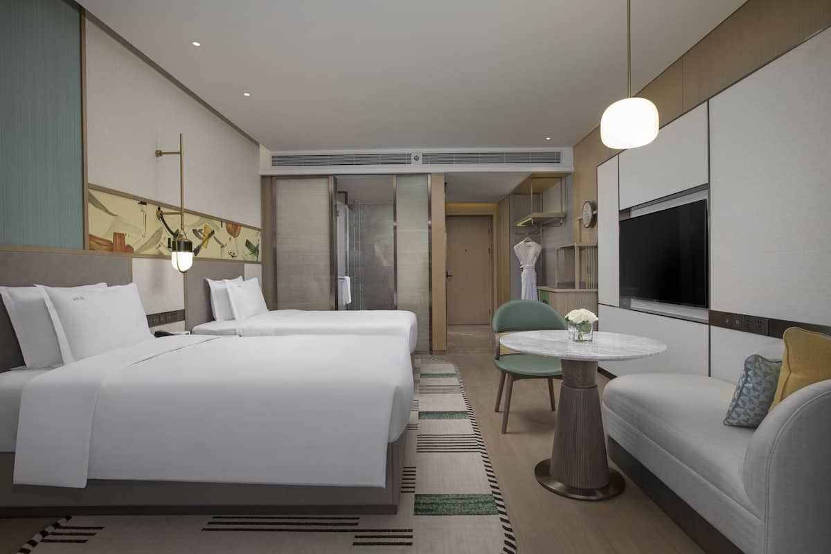 A hotel room with two beds, a sofa, a round table, and a TV.