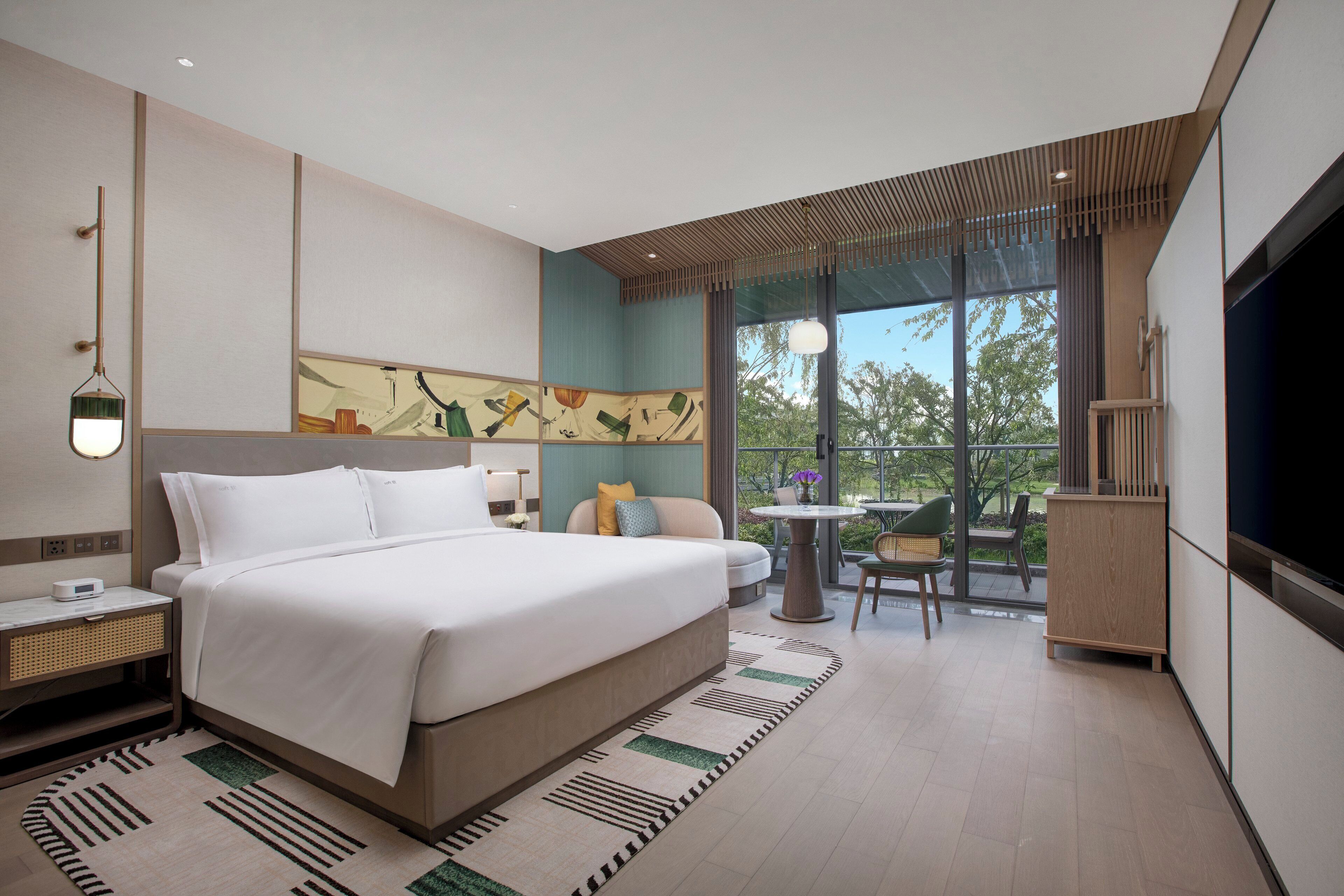 Una habitación de hotel moderna con una cama grande, un área de comedor con mesa y sillas, y un televisor.