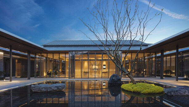 Un edificio moderno con fachada de vidrio, un estanque reflectante y un árbol en primer plano.