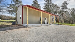 A covered outdoor area with a gravel floor, a wooden bench, and a small table. - Eureka Springs Area Home w/ Porch, Grill! (Berryville)